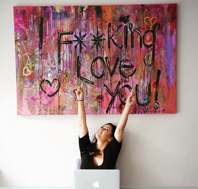 Woman in front of a coloruful abstract painting with text on a white wall.